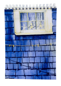 A blue shingled house with a white lace curtain window with 3 white starfish in the window and a clothesline with a shadow on the blue wall.