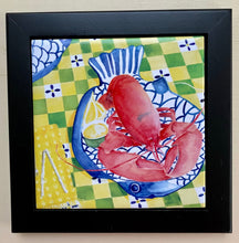 Load image into Gallery viewer, on a yellow, white and green checked tablecloth sits a blue and white large fish shaped dish with a cooked red lobster with hot butter and a wedge of lemon off to the side. Surrounded by a black wooden frame