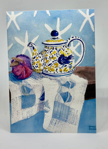 A yellow, white and blue teapot with a blue bird motif.  There is a red onion for color and interest as well as star fish images against a blue wall.