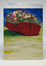 Load image into Gallery viewer, A red dory filled to bursting with petunias.  The gunnels are painting a dark green and are enhanced by a string of lights that are lite each evening during the summer.