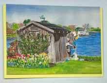 Load image into Gallery viewer, A New Castle, NH Garden Shed by the water with Tulips and lawn.  The shed is weathered wood with an old wooden lobster trap hanging on the side filled with lobster buoys that had washed up on shore.