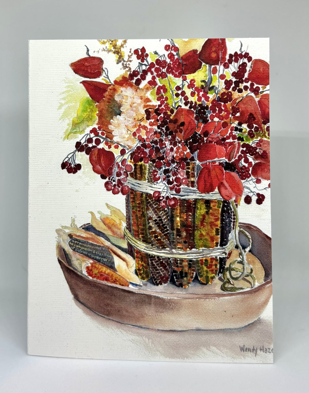 Multicolored Indian Corn ted in two spots with twin to hold it all around a glass vase on the inside.  Then dried flowers are placed inside with some corn laying on the table within a wooden round tray.