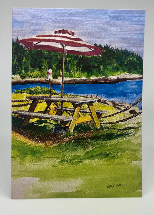 McLoon's Lobster Shack Picnic Table by the working harbor.  There is grass surrounding the table with a well worn path created by the many diners.  The red and white umbrella is a perfect foil for redirecting the sun.  This season opens May 24, 2025!  Bon Appétit!