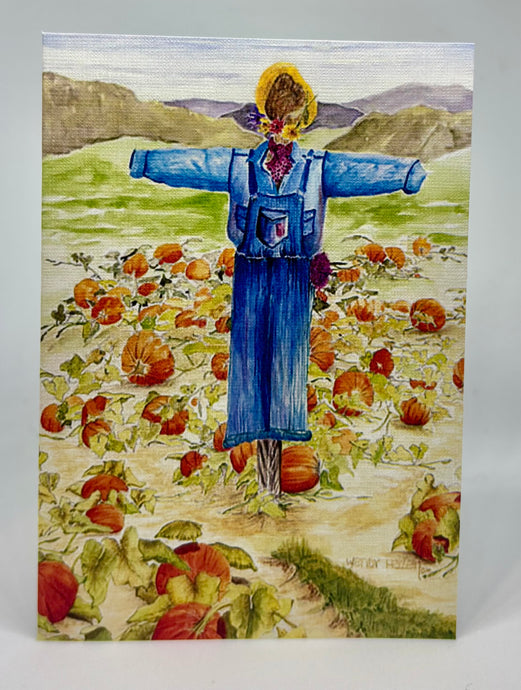 It is a field of pumpkins with a scarecrow in the middle dressed in blue overalls, blue work shirt and a straw hat with a red caveat.  It is end of season and with the mountains in the background the first frost is on the horizon.