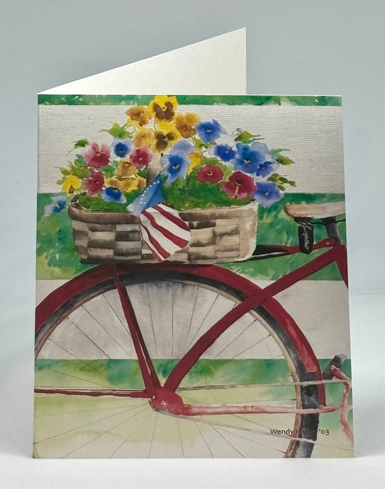 It is a red 'cruiser' bike with a basket of pansies behind the seat leaning against a white wooden fence.  This is located in West Barnstable on Cape Cod.