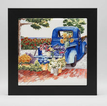 Load image into Gallery viewer, Framed artwork of a blue truck with flowers on brick walkways and cobblestone street background with a view to the sea.