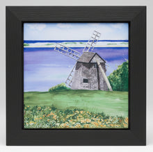 Load image into Gallery viewer, A ceramic tile of a windmill in a field with flowers, trees and water with a dune in the background.  The tile is placed in a black wooden frame.